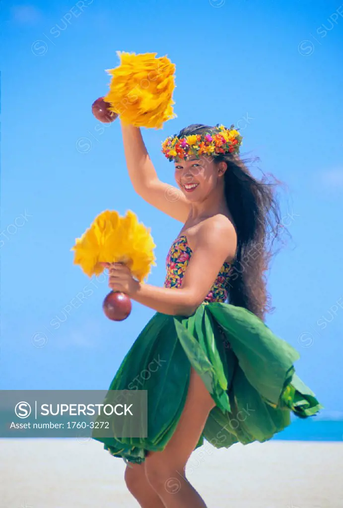 Smiling young woman hula w/ ´uli´uli in ti leaf skirt, beach w/ blue sky C1466