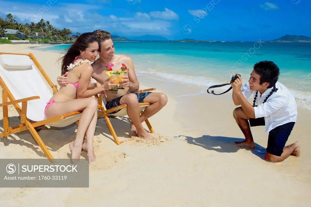 Hawaii, Oahu, Lanikai, A Beachboy Takes A Picture Of A Young Couple On The Beach.