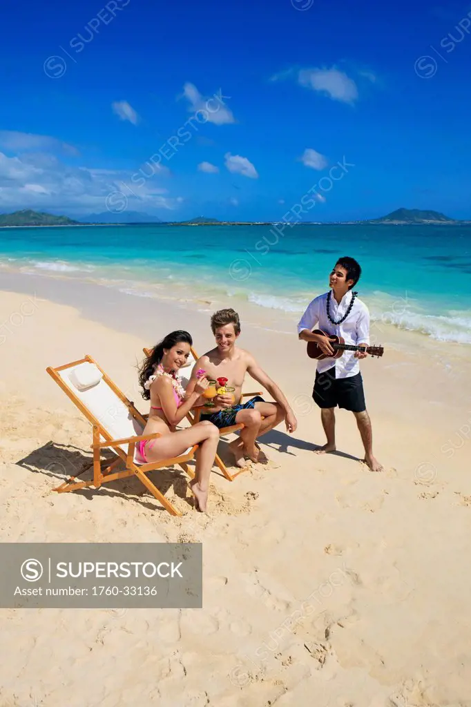 Hawaii, A Man Plays Ukulele For A Young Couple On The Beach.
