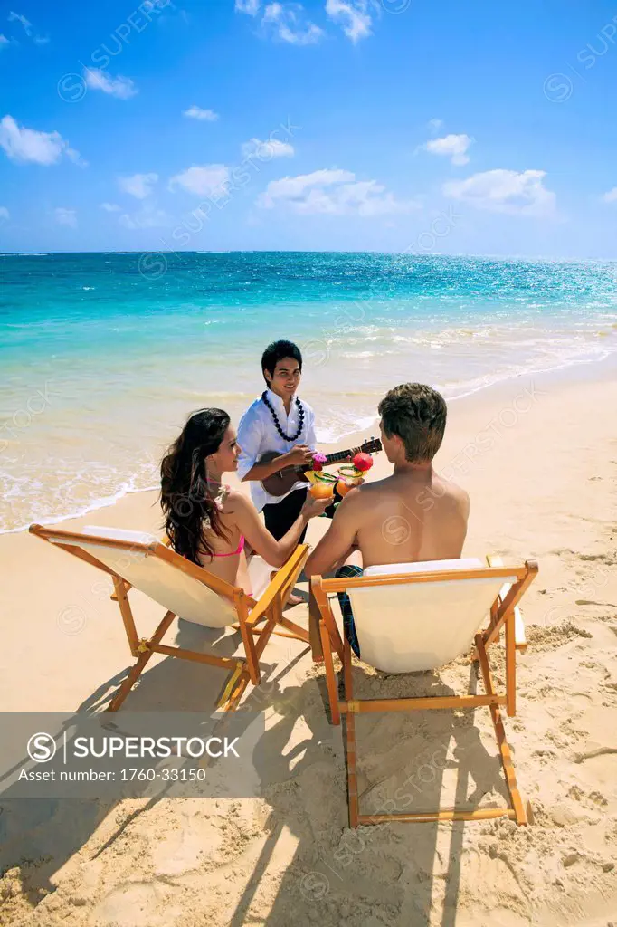 Hawaii, Polynesian Man Plays Ukulele For A Young Couple On The Beach.