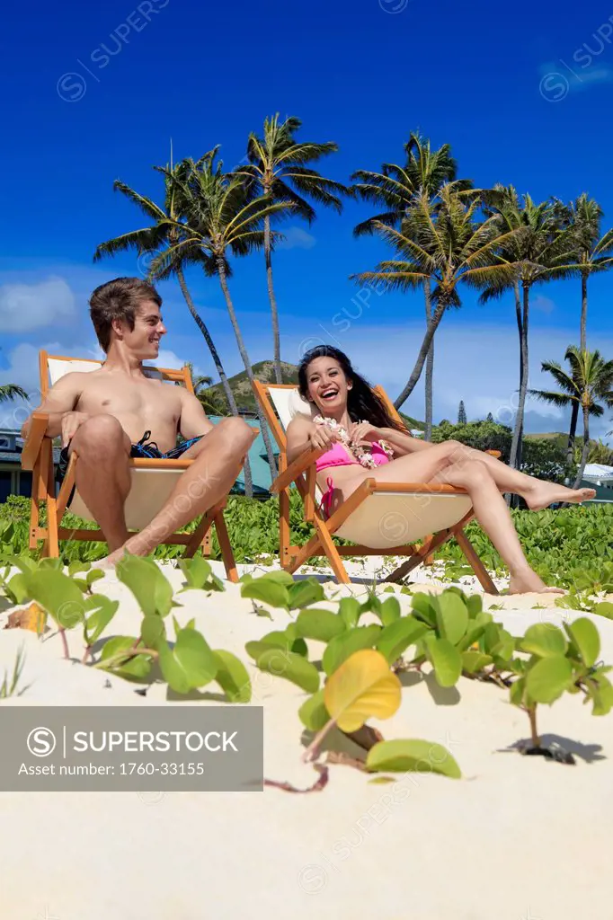 Hawaii, A Young Couple In Lounge Chairs At The Beach.