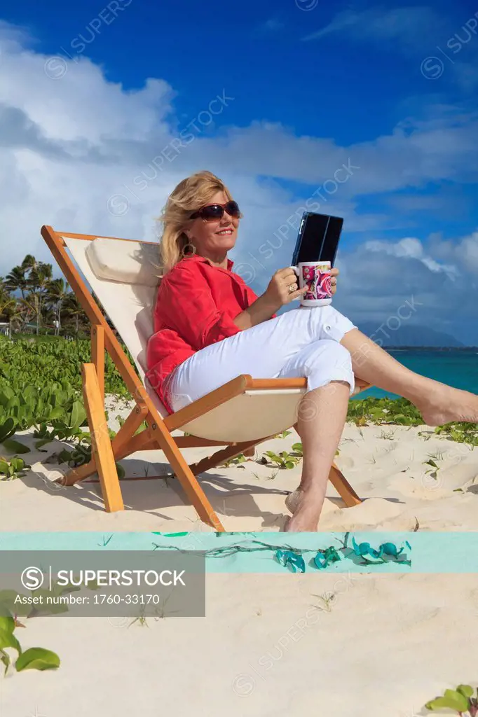 Woman On Beach Uses Electronic Tablet.
