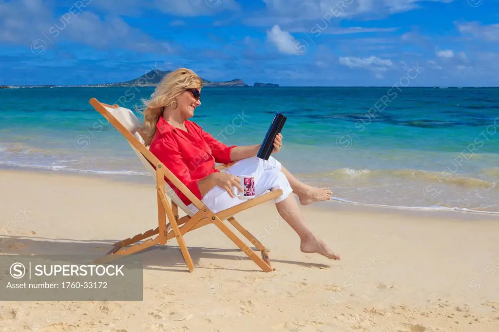 Woman On Beach Uses Electronic Tablet.