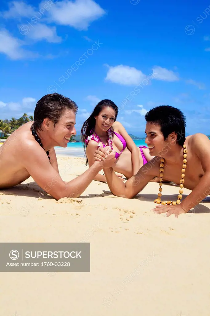 Hawaii, Two Young Men Arm Wrestling On The Beach While Girl Watches.