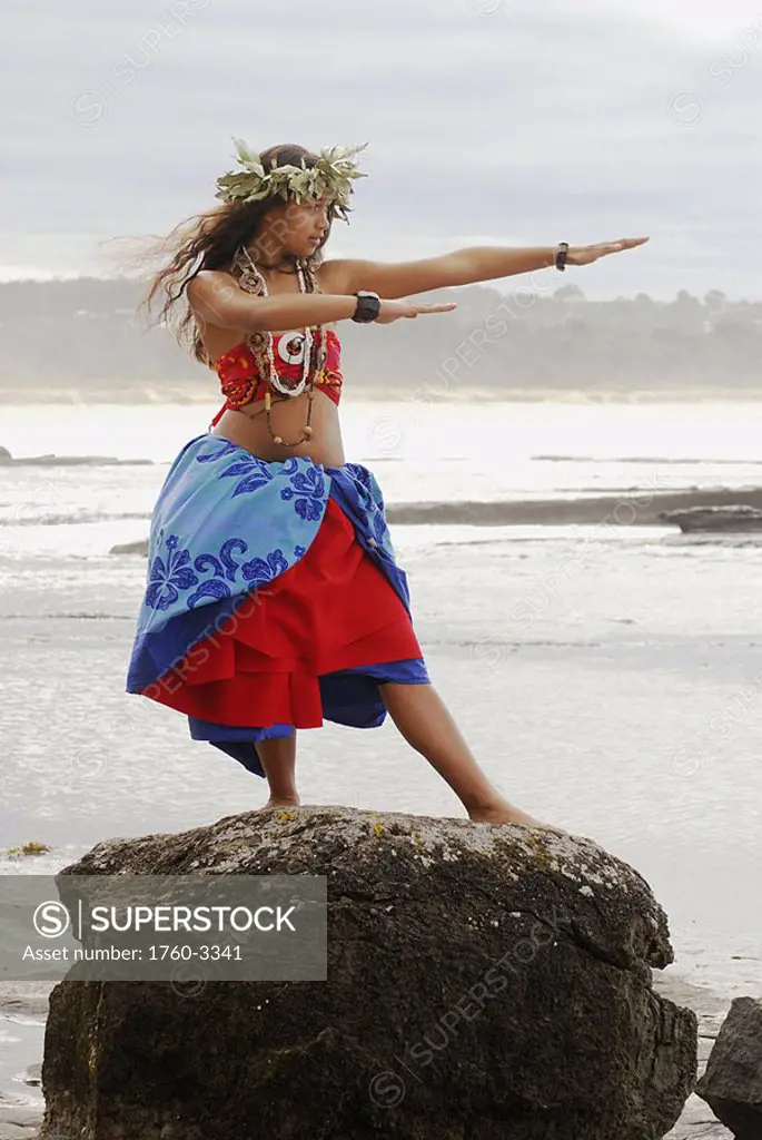 Beautiful Hawaiian girl dancing hula on a rock overlooking the ocean