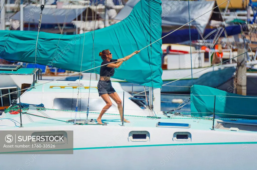 Hawaii, Oahu, Waikiki, Ala Wai, Woman raising the sail on her yacht.