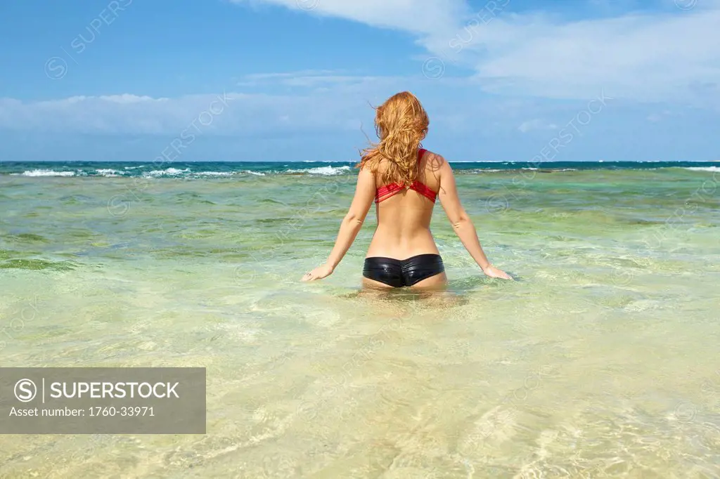 A young woman in a bikini enters the ocean water; Wailua, Hawaii, United States of America