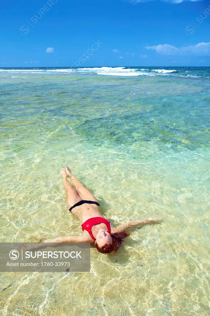A young woman lays in the shallow ocean water; Wailua, Hawaii, United States of America