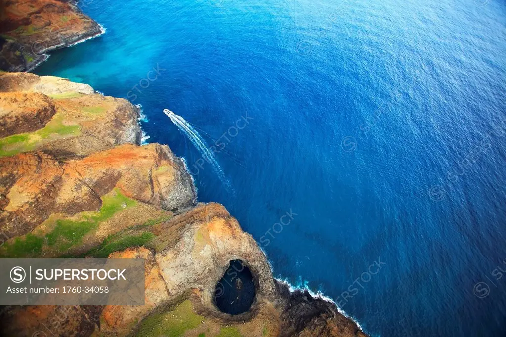 Aerial view of the rugged coastline and a boat in the pacific ocean along an hawaiian island; Hawaii, United States of America