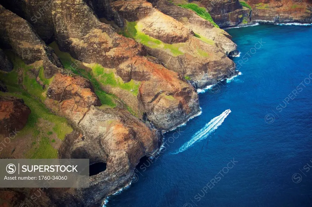 Aerial view of the rugged coastline and a boat in the pacific ocean along an hawaiian island; Hawaii, United States of America