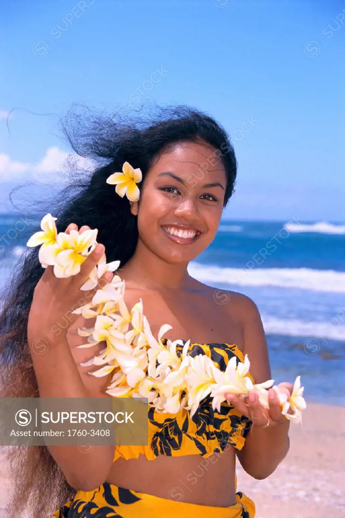 Polynesian smiling woman w/ plumeria in hair, holding lei in hand, on beach C1494