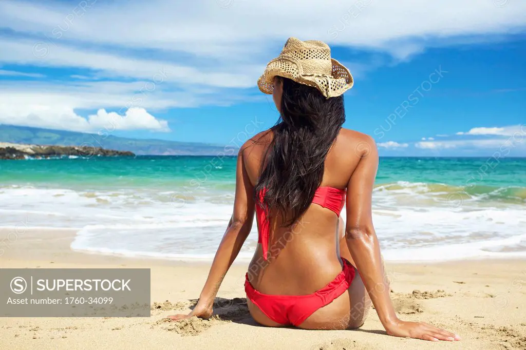 A young woman in a red bikini sitting on the beach of an hawaiian island; Maui, Hawaii, United States of America