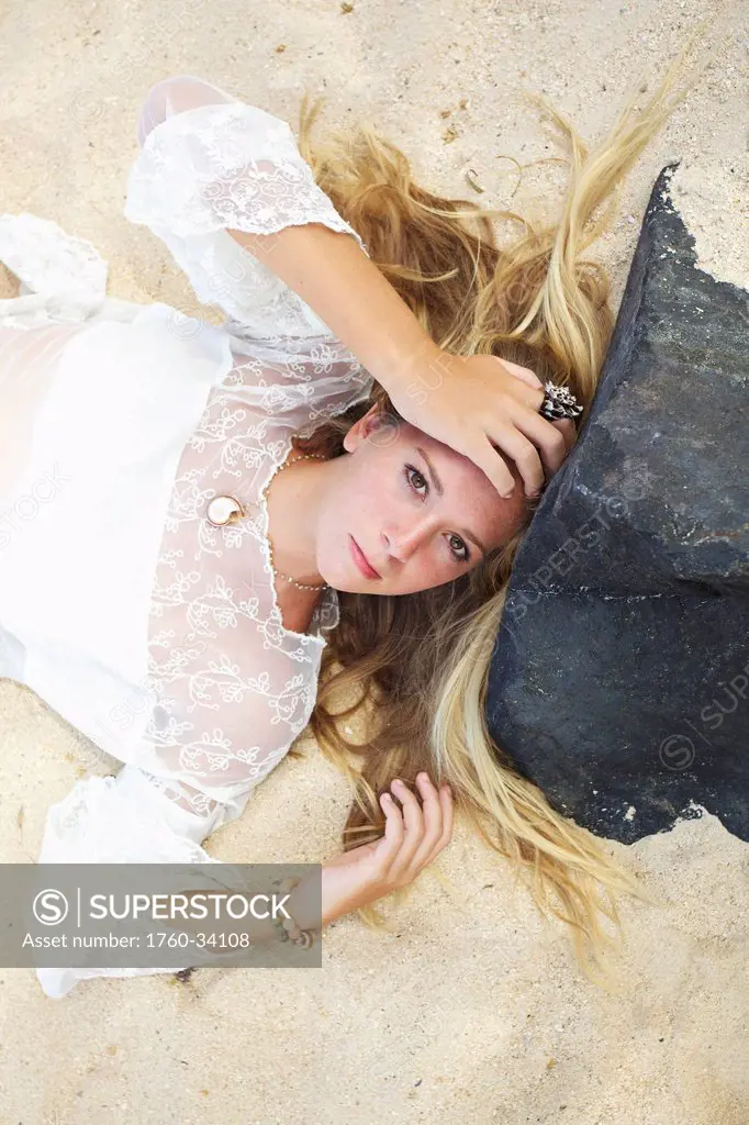 A young woman with long blond hair and a white sheer top posing on a beach; Maui, Hawaii, United States of America