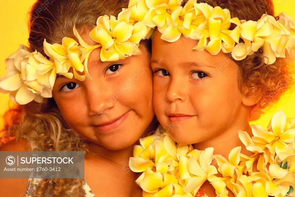 Closeup of two girls wearing plumeria leis & haku, cheeks together, smiling C1491