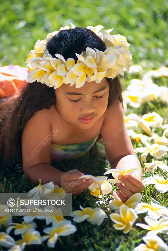 Closeup of little Hawaiian girl laying on grass with plumeria flowers C1460