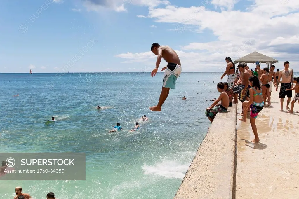 A boy jumping off the Waikiki Wall; Waikiki, Oahu, Hawaii, United States of America