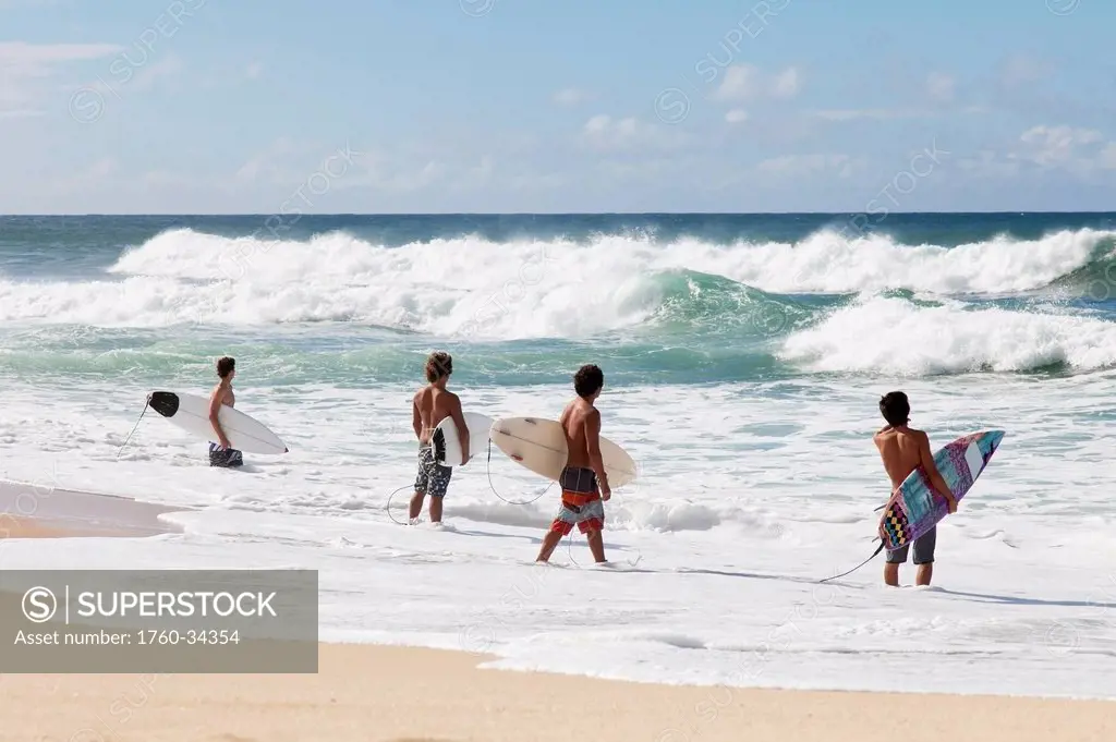 Four young surfers check out the incoming waves; Oahu, Hawaii, United States of America