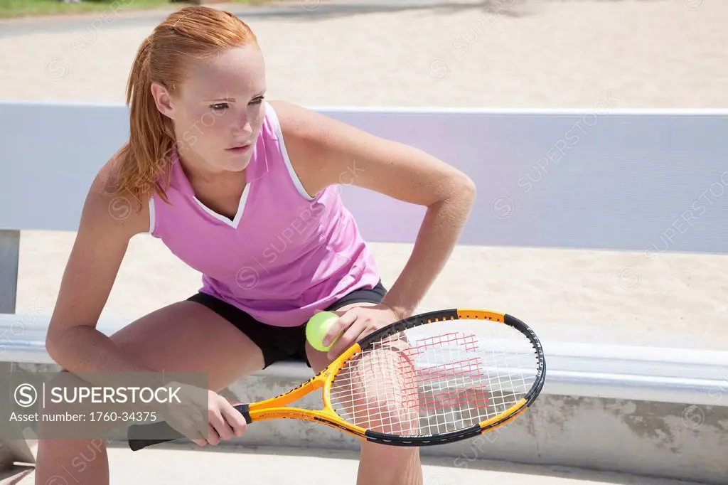 A girl sitting on a bench with a tennis ball and racquet; Oahu, Hawaii, United States of America