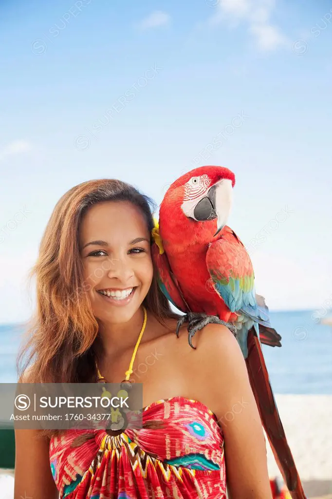 Portrait of a woman holding a colourful bird on her shoulder; Waikiki, Oahu, Hawaii, United States of America