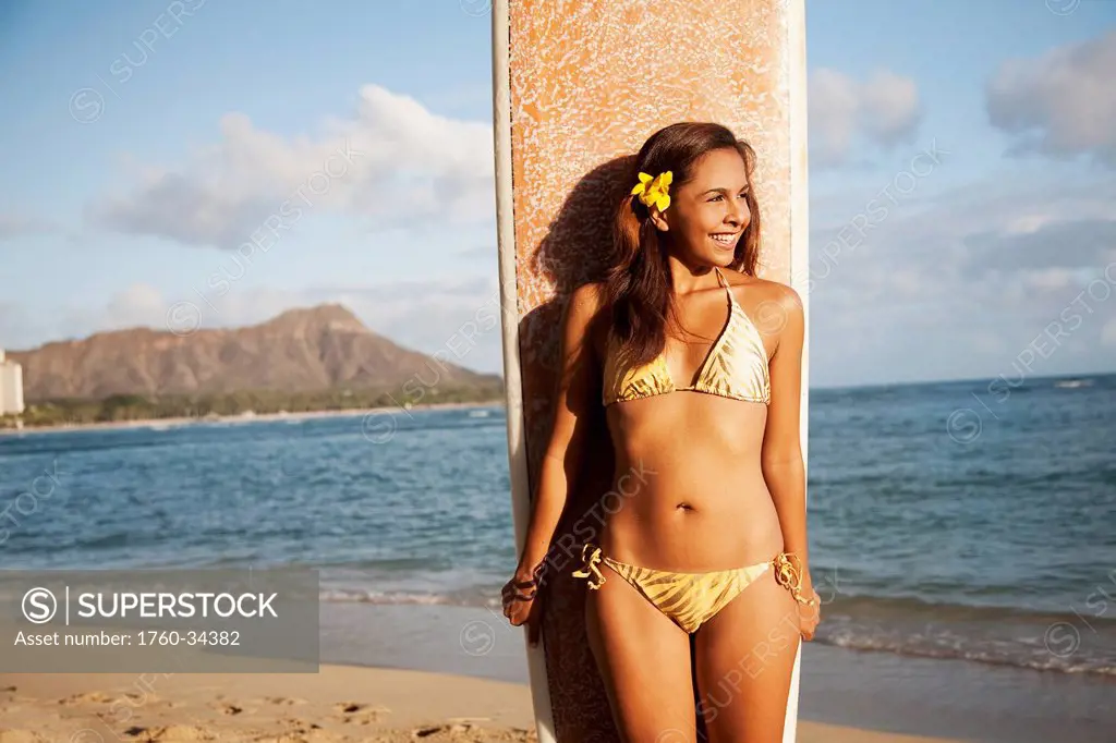 Portrait of a woman on a beach in a bikini holding a surfboard; Waikiki, Oahu, Hawaii, United States of America