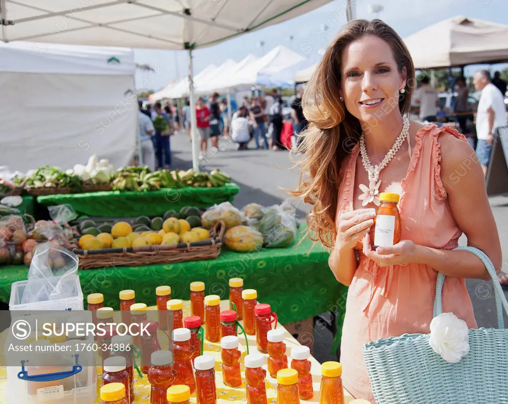 A woman selecting honey to purchase at an outdoor market; Honolulu, Oahu, Hawaii, United States of America