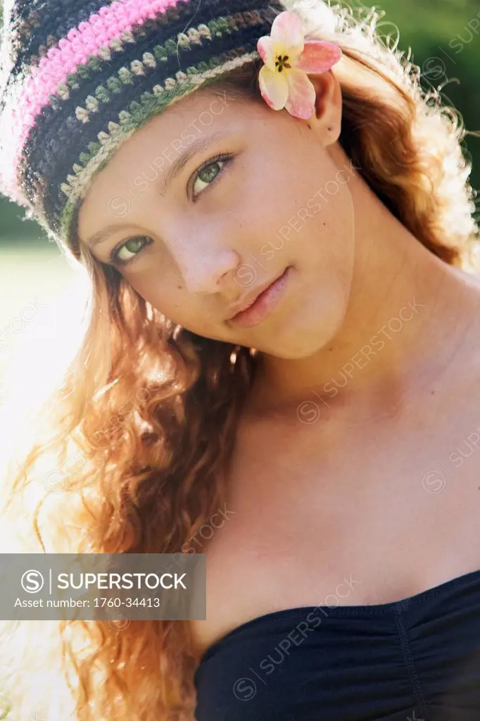 Portrait of a young woman with long blond hair with a knit hat and tropical flower accessory; Oahu, Hawaii, United States of America