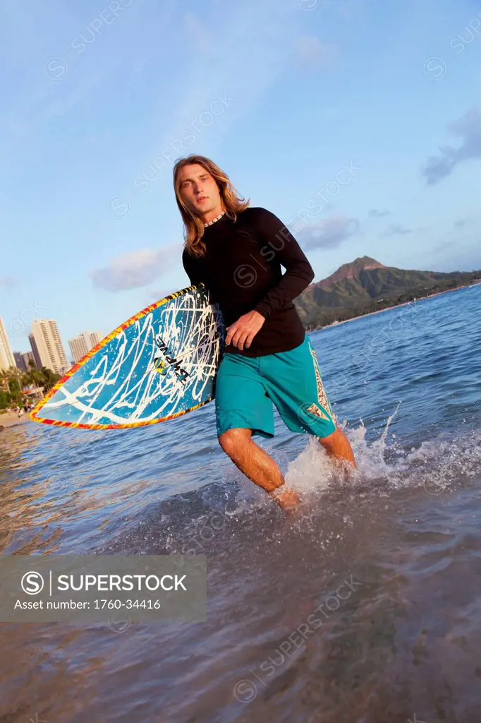 A surfer carrying his surfboard and walking in shallow water; Waikiki, Oahu, Hawaii, United States of America