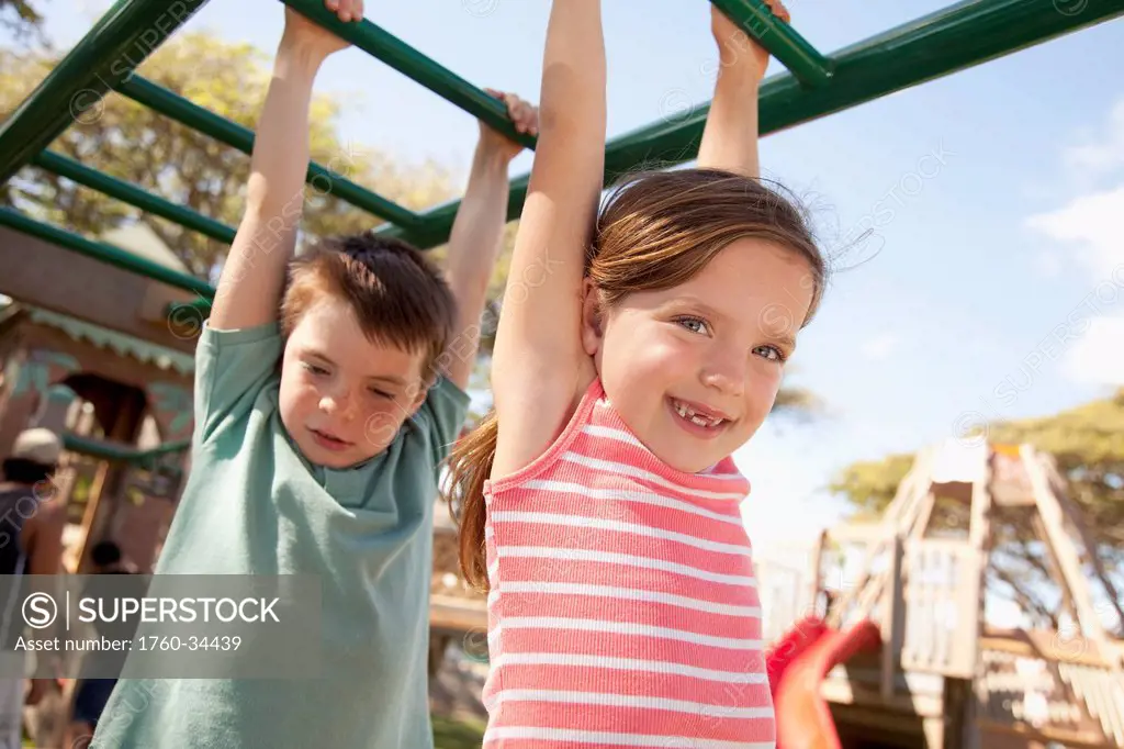 Brother and sister play on monkeybars at playground; Oahu, Hawaii, United States of America