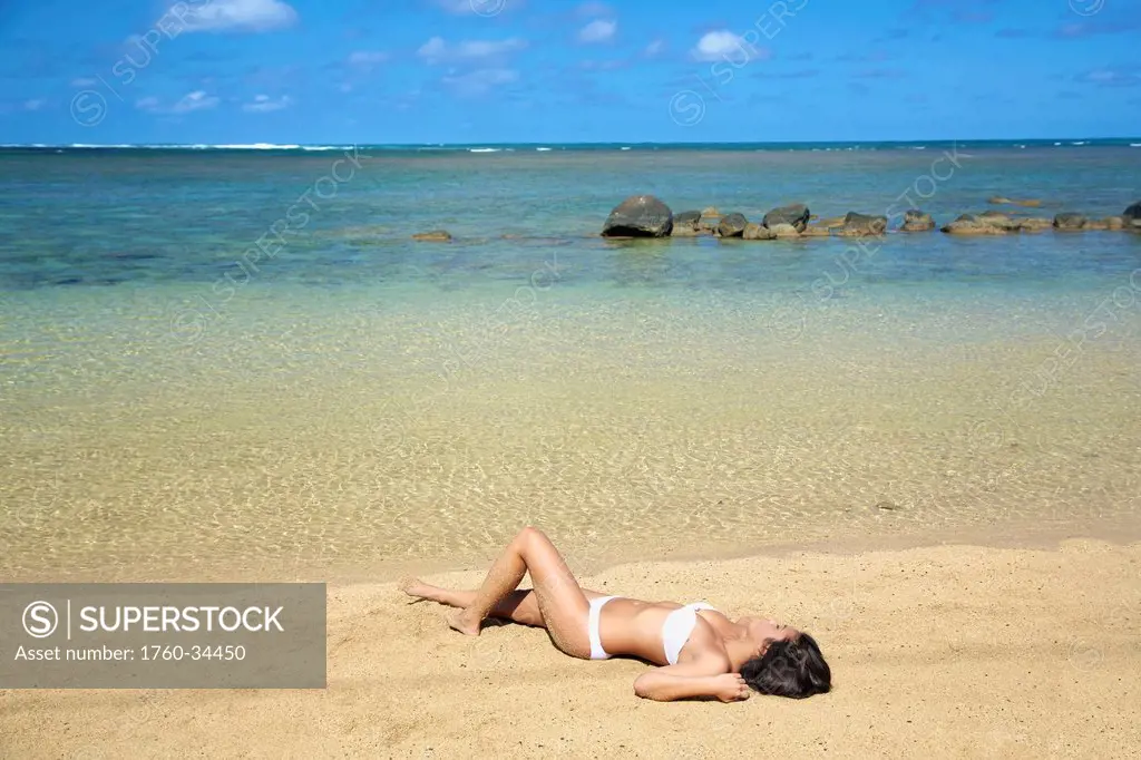 Woman in strapless white bathing suit laying out on the beach; Kauai, Hawaii, United States of America