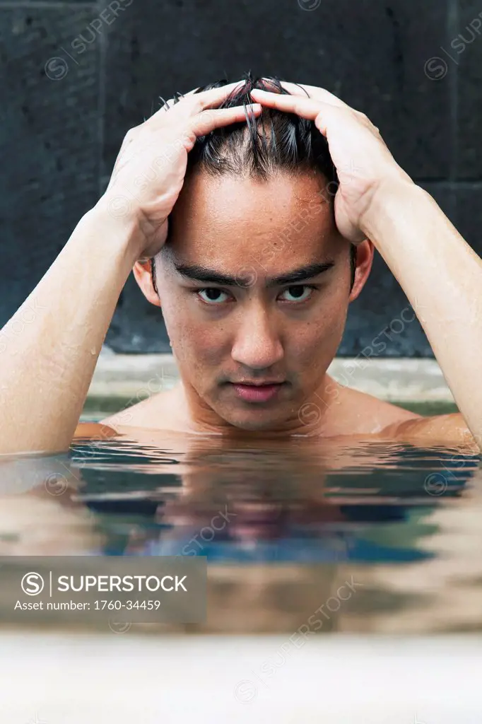 A young man sitting by the edge of the pool holding his head in his hands; Honolulu, Oahu, Hawaii, United States of America
