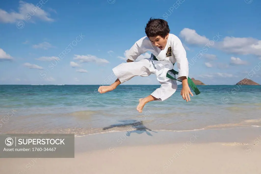 A boy in a martial arts uniform leaping on a beach; Honolulu, Oahu, Hawaii, United States of America