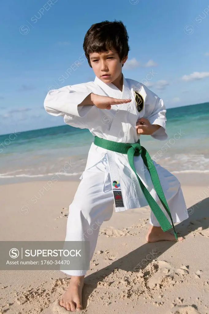 A young boy in a martial arts uniform on a beach; Honolulu, Oahu, Hawaii, United States of America
