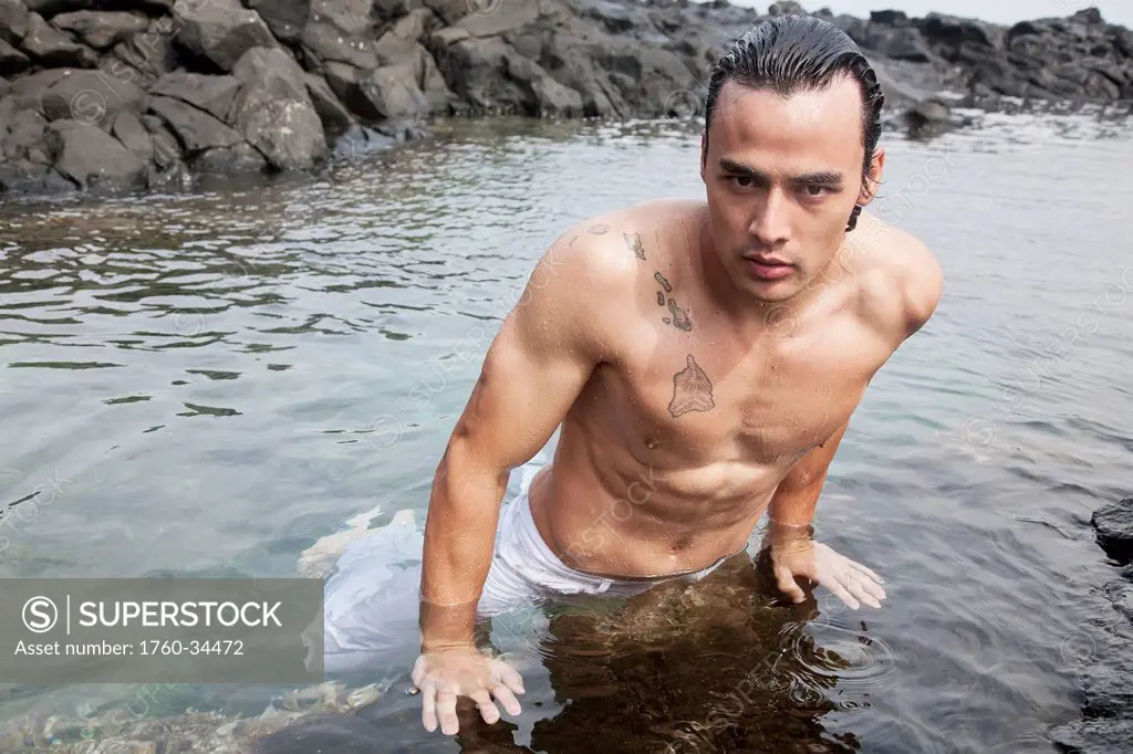 A shirtless man on a rock ledge in the water; Honolulu, Oahu, Hawaii, United States of America