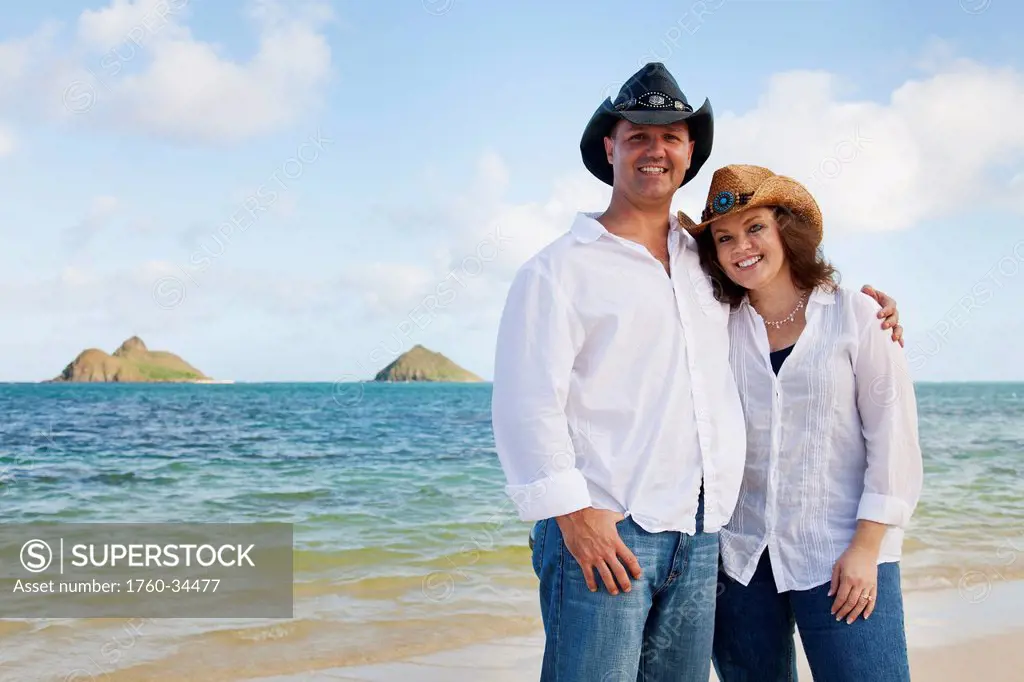 Portrait of a couple in white shirts and western hats standing on the beach; Honolulu, Oahu, Hawaii, United States of America
