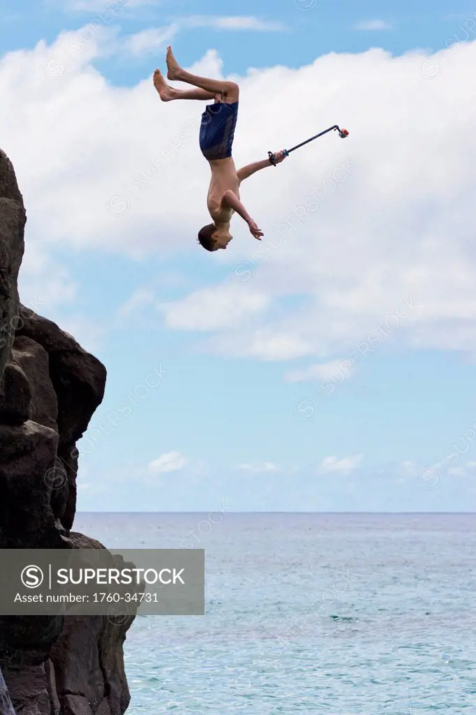 A young man enjoys a 30 foot high jump at da big rock in Waimea Bay; North Shore, Oahu, Hawaii, United States of America