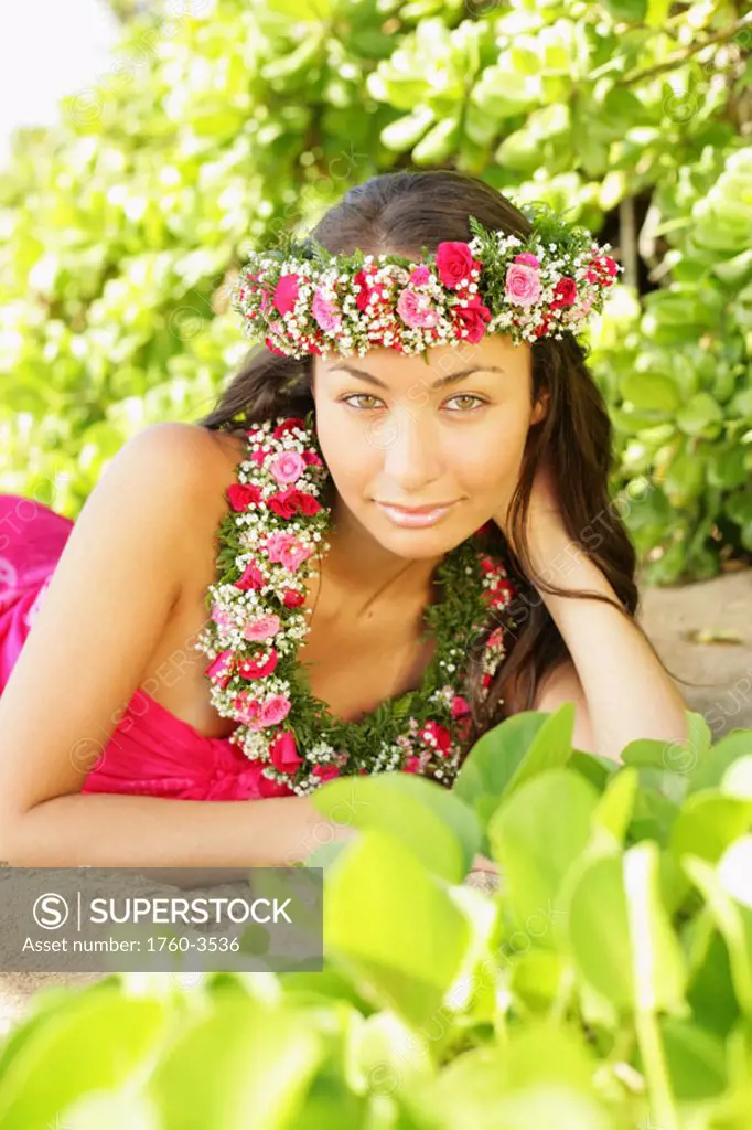 Hawaii, Local girl laying on sand wearing flower leis surrounded by bright vegetation.