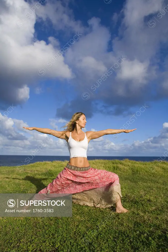 Hawaii, Maui, young woman doing yoga on grassy hill next to the ocean.