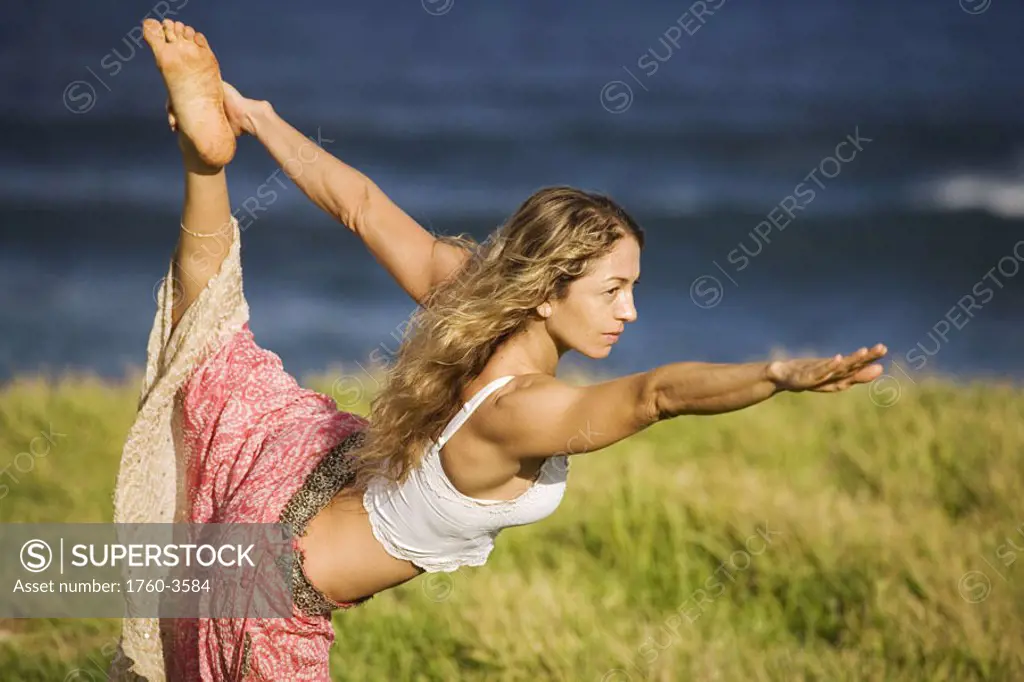 Hawaii, Maui, young woman doing yoga on grassy hill next to the ocean.