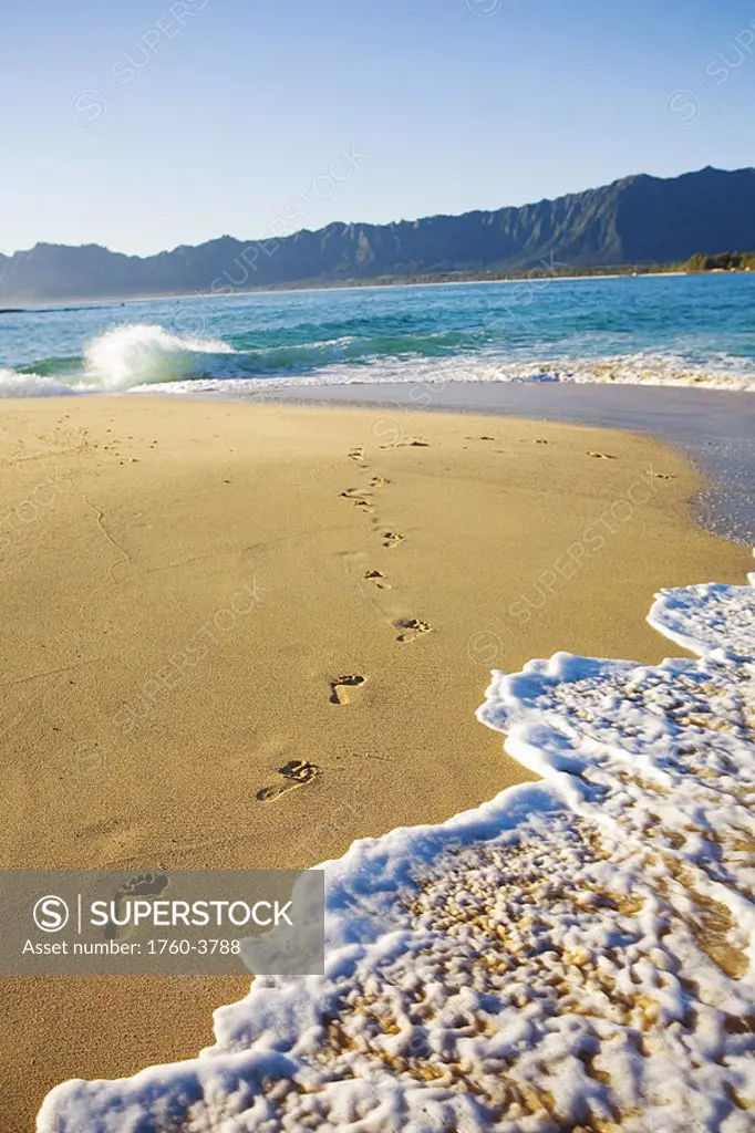 Hawaii, Oahu, Mokulua Island, footprints in the sand, water lapping on the beach, Koolau mountains in background