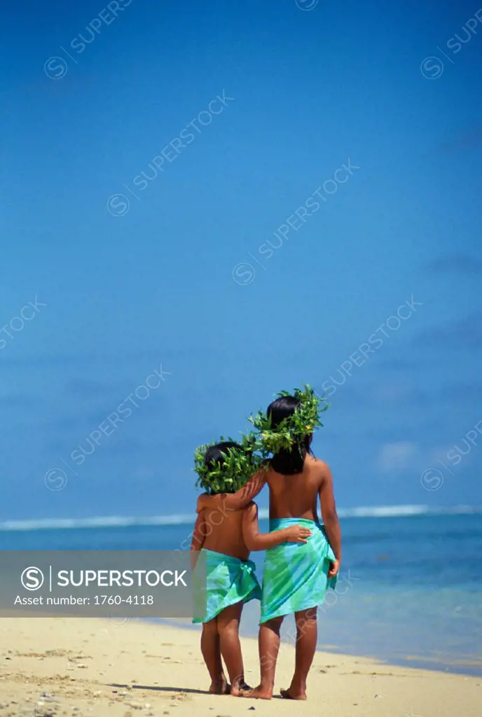 Little Polynesian sisters in haku and pareo on beach face water, view from behind