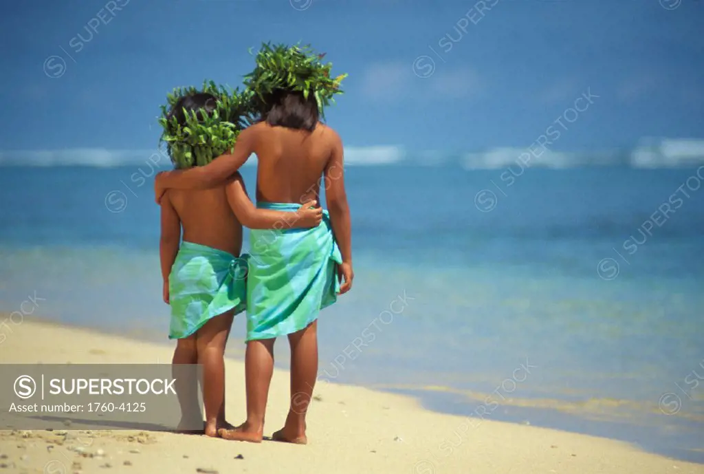 Two Polynesian girls pareo and haku leis face water, arms around each other, behind