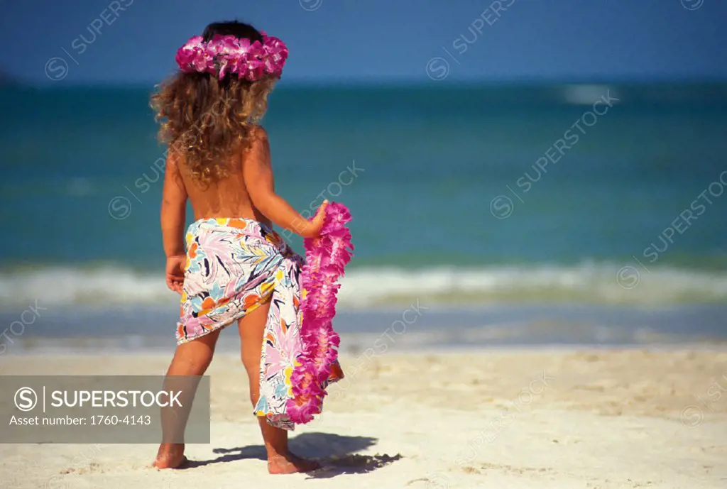 Back view of little girl at the beach, holding pink lei and wearing a pareo