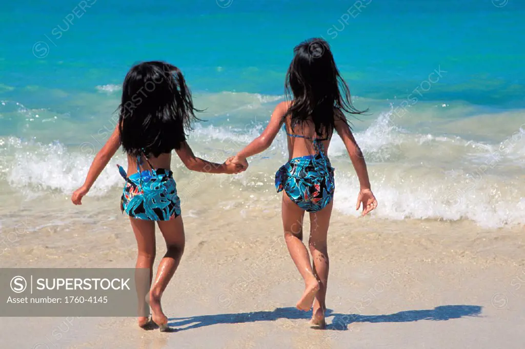 Hawaiian girls running into shoreline, view from behind, matching outfits