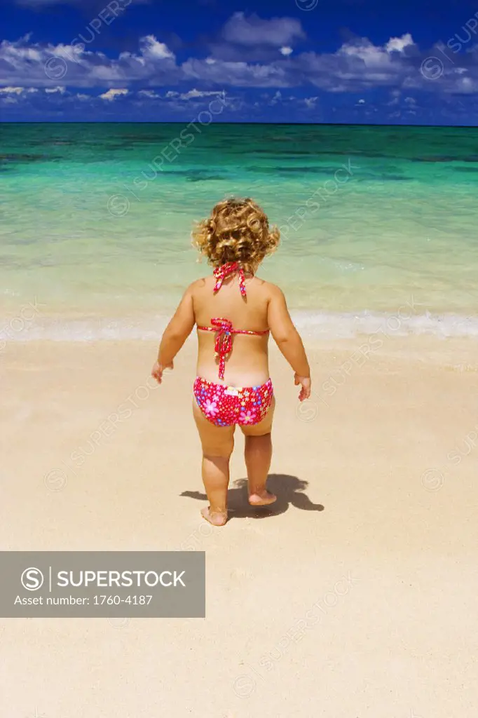 Little girl with blond curly hair plays on the beach