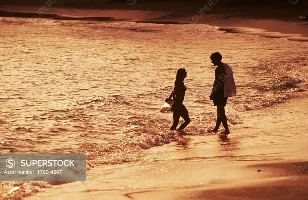 Caribbean, Couple wading in ocean along beach at sunset