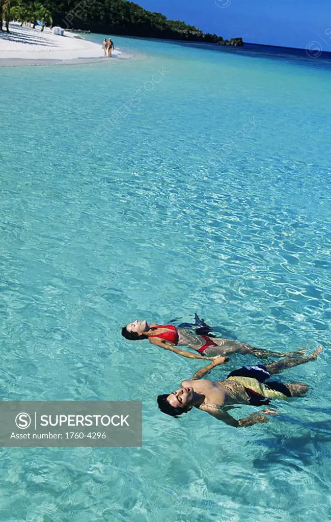 Caribbean, Honduras, The Bay Islands, Couple floating in clear turquoise ocean water, Beach in distance