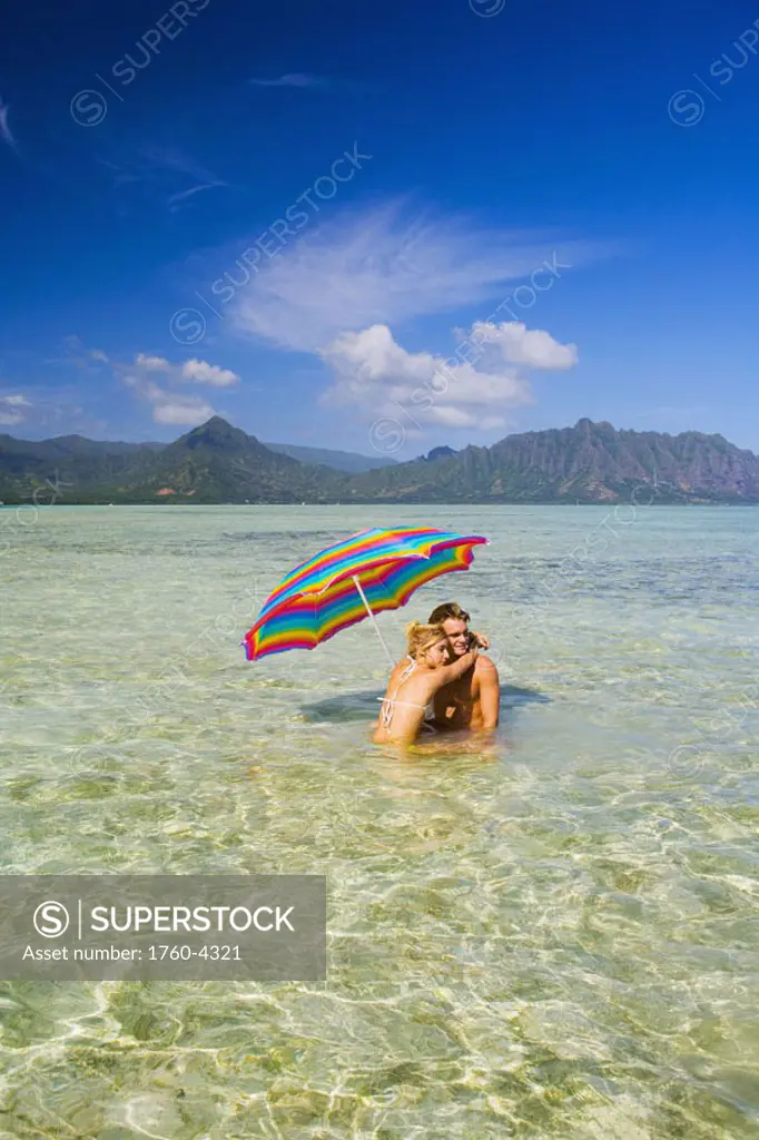 Hawaii, Oahu, Kaneohe, couple under a brightly colored umbrella in crystal clear water at the sandbar or ´dissapearing island´