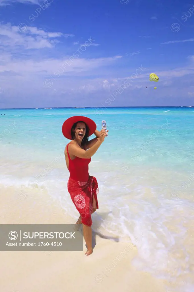 Mexico, Cancun, woman in red on beach taking self portrait with cell phone.