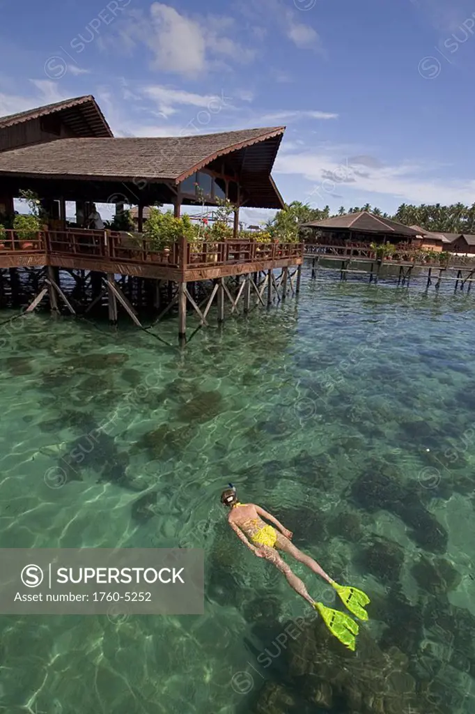 Malaysia, Mabul Island, Sipidan Water Village, Woman snorkels over coral reef below resort