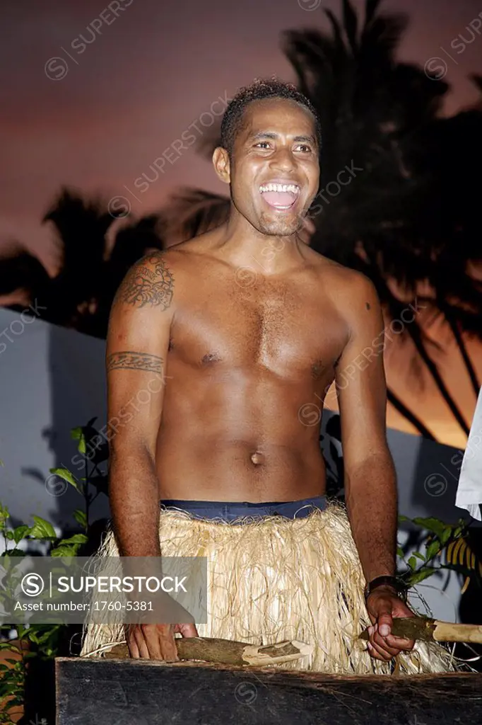 Fiji, Viti Levu, Coral Coast, Hideaway Resort, Fijian drummer in traditional grass skirt in tropical setting at sunset